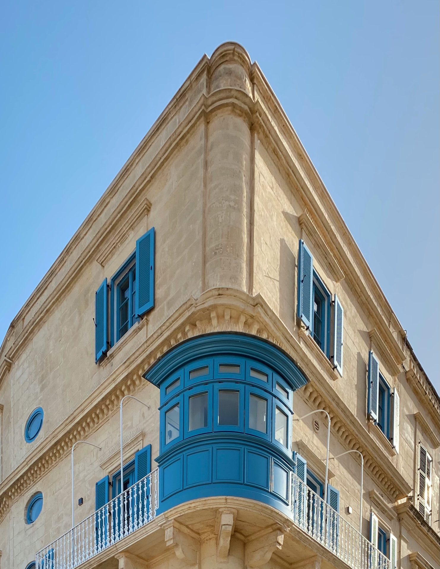 A sunlit Maltese corner building with traditional blue shutters and balcony