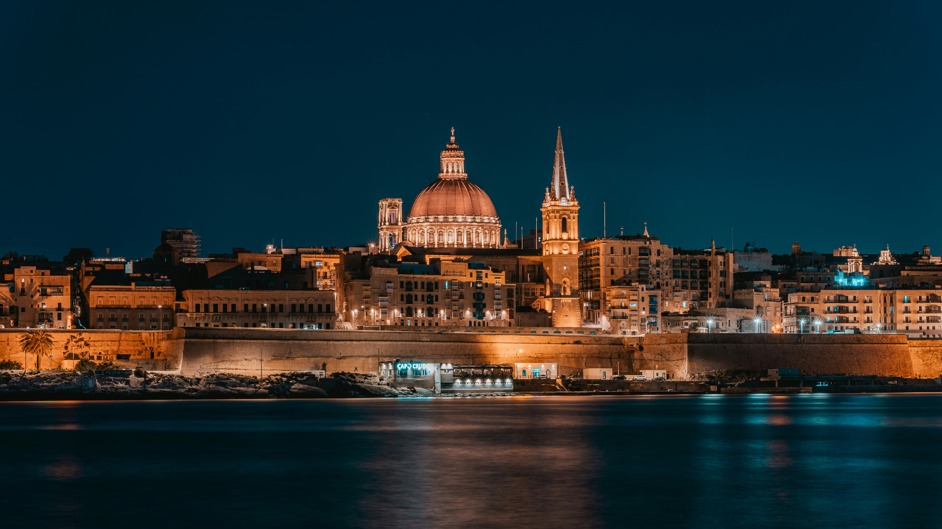 Valletta skyline at night with the illuminated dome and spire reflected on the water